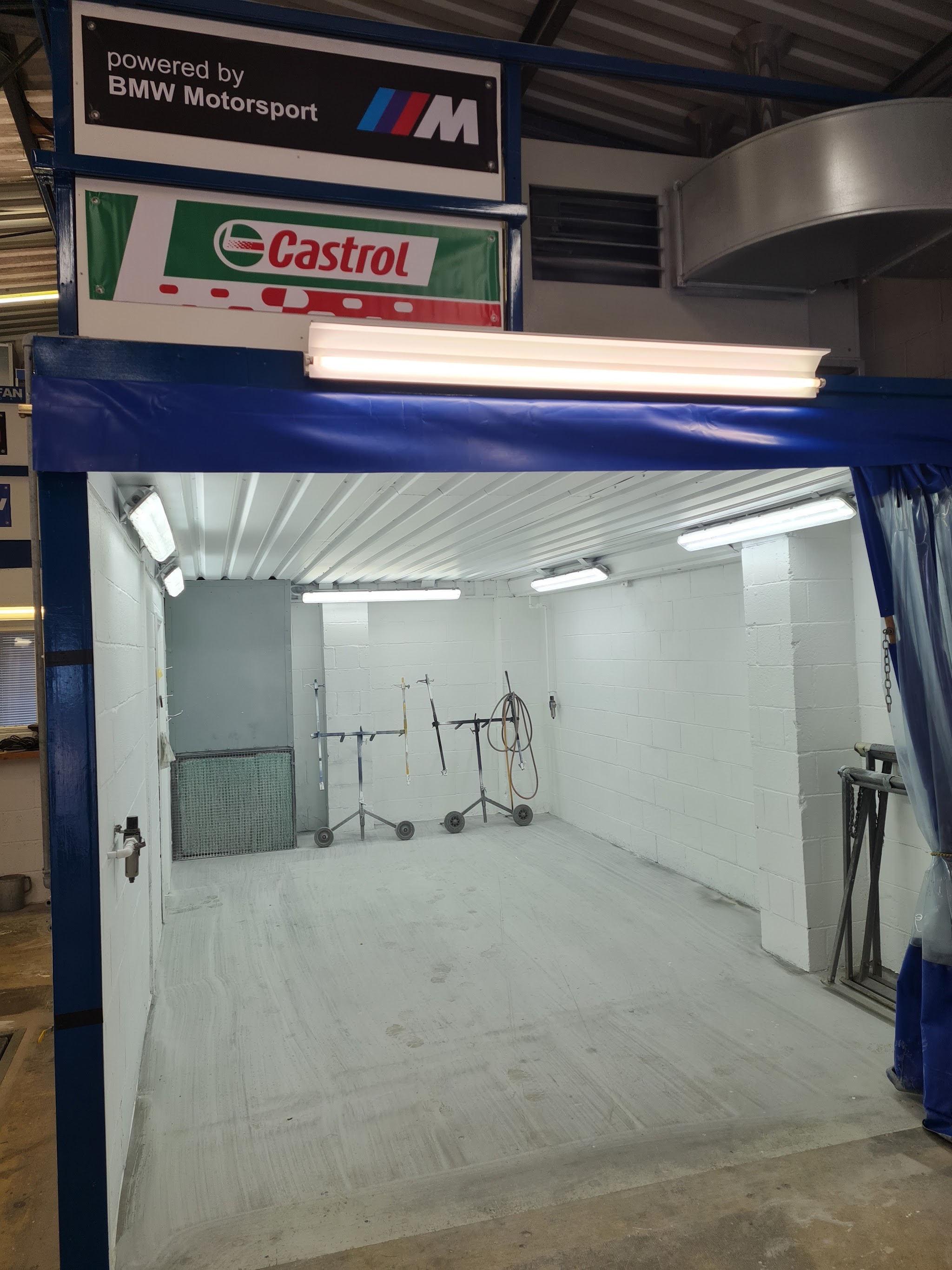 The spray booth with its doors open, blue frame and strip lights, ready for the next car