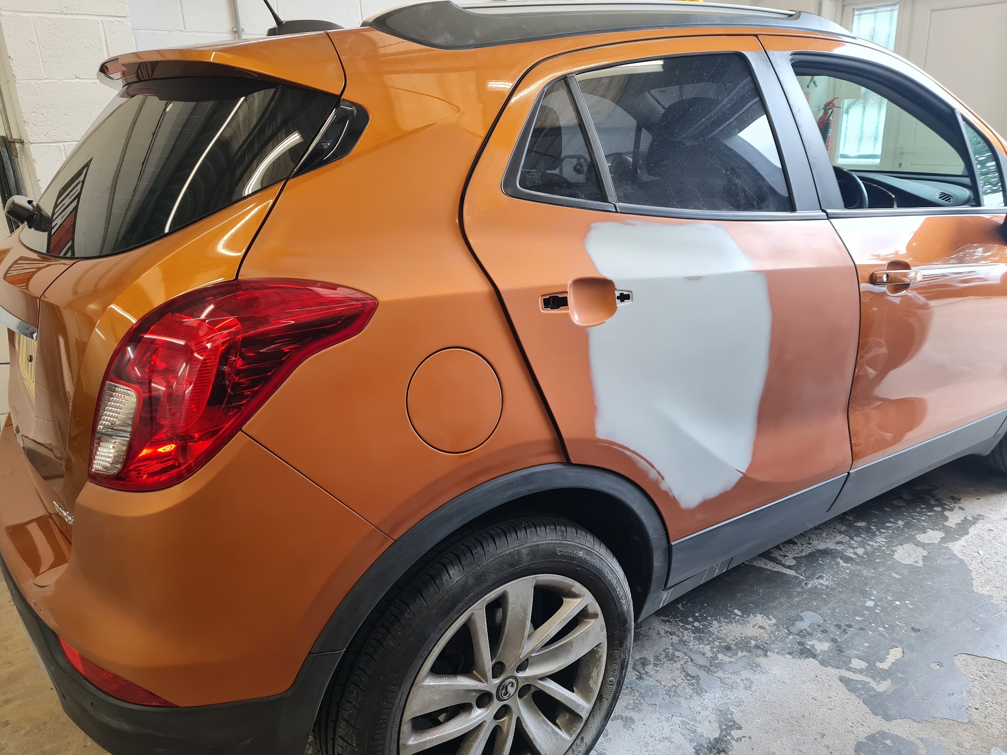 Orange Vauxhall Mokka in the workshop with its rear door in grey primer