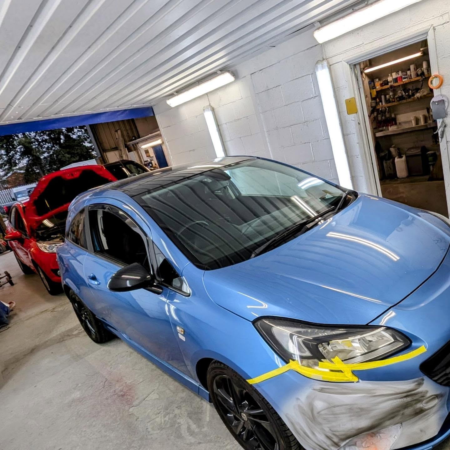 Blue Vauxhall Corsa masked up in the workshop with its front bumper being prepared