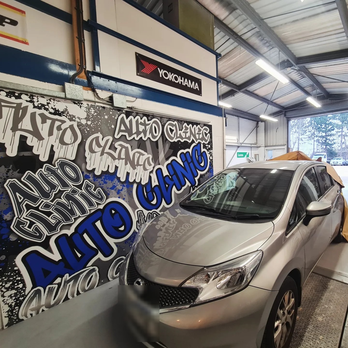 The graffiti Auto Clinic mural on the workshop wall, blue, black and white, with a car parked in front