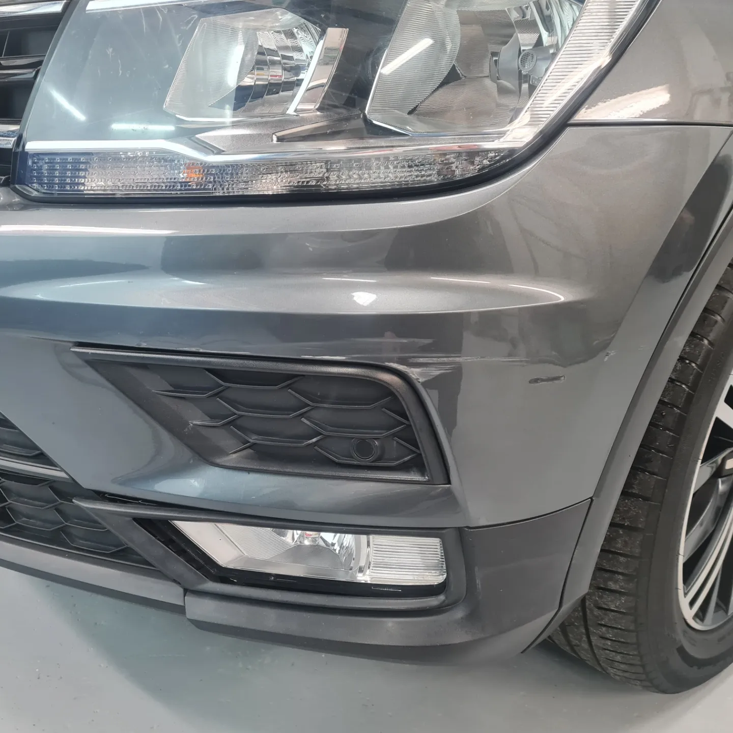 Grey Volkswagen front bumper corner with scuffs below the headlight